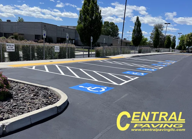 Freshly paved accessible parking stalls with blue ADA symbols and white striping at a commercial site