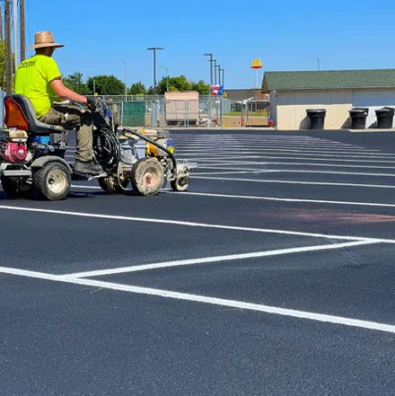 Crew member striping a parking lot with a ride-on line painter