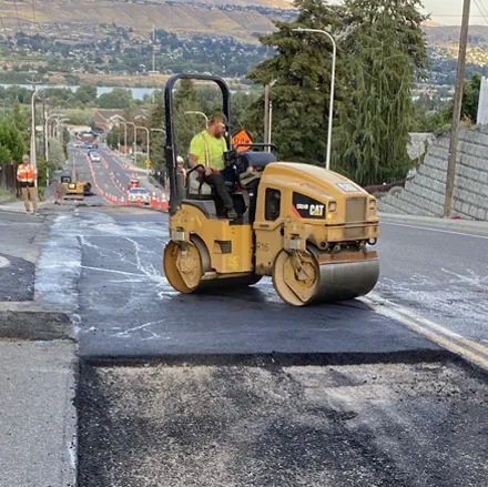 Crew member repairing damaged asphalt with a small roller